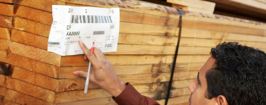 Worker inspecting a barcode label on a stack of lumber for inventory tracking and supply chain management.