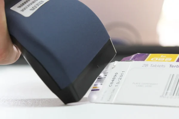 Axicon 6000W Pharmacode Verifier scanning a pharmaceutical barcode on medication packaging.