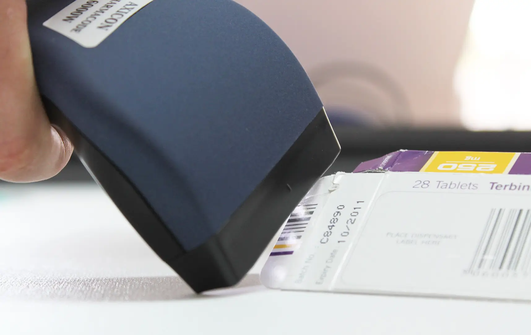Axicon 6000W Pharmacode Verifier scanning a pharmaceutical barcode on medication packaging.